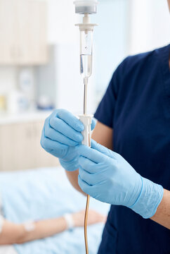 Nurse adjusting IV drip with gloved hands in a hospital room  