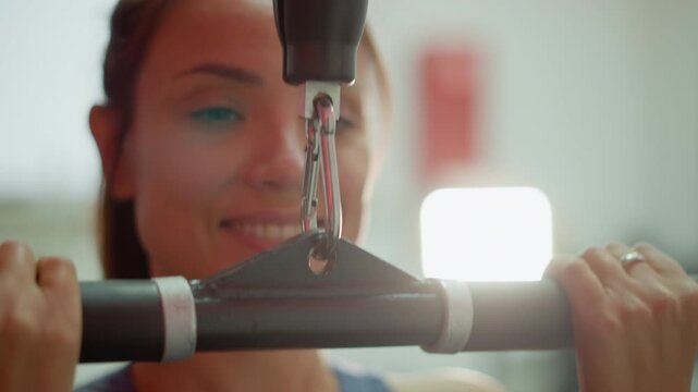 Woman performs pull ups on gymnastic bar in gym. Close up view shows upper body movement and interaction with exercise equipment indoors. Bright lighting illuminates scene