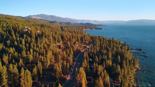 Forest slopes extend along the shore of Lake Tahoe. Green and gold conifers border blue water with mountain ridges fading into the distance.