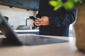 Fototapeta premium Person holding smartphone while working from home, staying connected and managing tasks in a modern kitchen, balancing personal and professional life