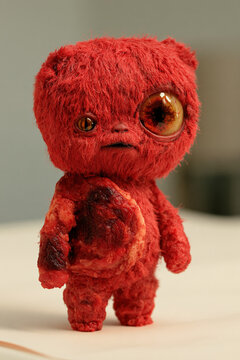 horror meat doll with shaggy red head, mismatched amber eyes and round exposed belly on pale tabletop, photorealistic