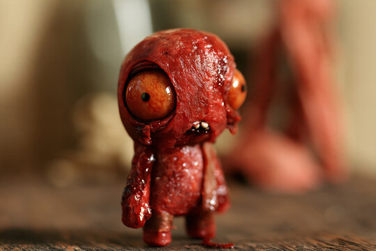 horror meat doll with smooth wet red head, huge orange eyes and tiny teeth in blurred warm room, photorealistic