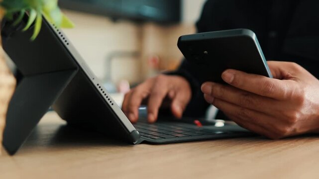 Businessman multitasking using smartphone and typing on digital tablet with keyboard for digital marketing project at the office