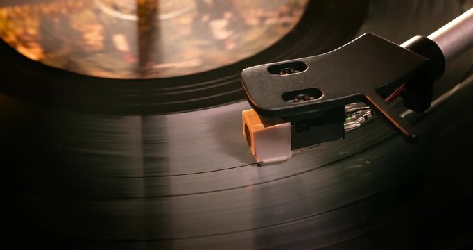 Detailed close-up of a turntable tonearm with white cartridge headshell, positioned over a black vinyl record on the platter, highlighting audio equipment precision.