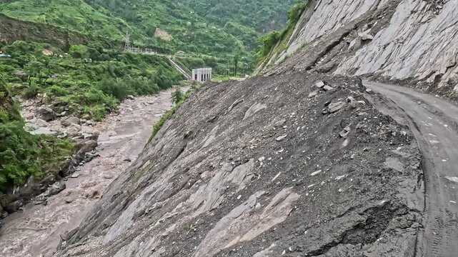 Bus moves dangerously on muddy, eroded mountain roads. Floodwaters rush below, threatening the route. Rocky slopes and green hills frame the perilous path
