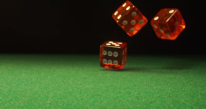 Dice fly and tumble toward the camera in extreme slow motion, landing on a green casino table with