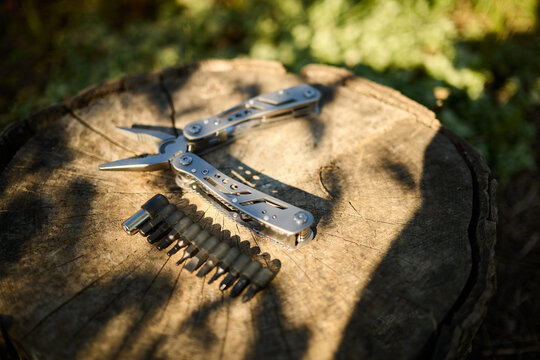 Multitool and screwdriver bits placed on a wooden stump in a garden during daylight