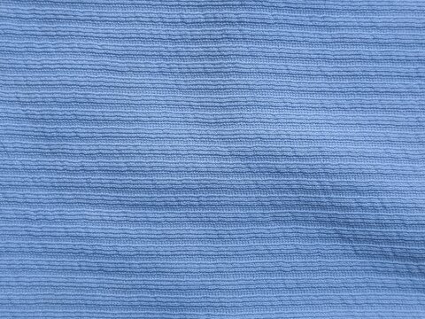 A detailed full frame close up shot capturing the ribbed texture and fine woven parallel lines of light blue fabric.