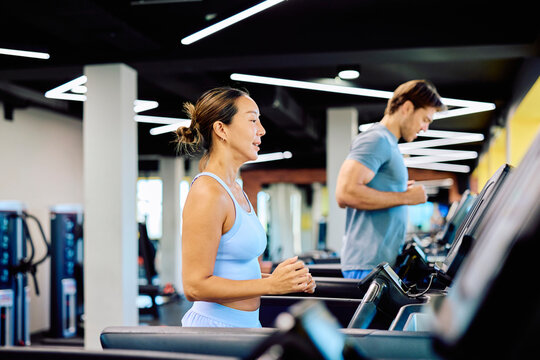 Woman and man running on treadmills, focusing on cardio fitness and healthy lifestyle at a modern indoor gym