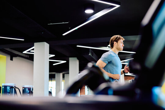 Man actively running on a treadmill, focusing on fitness and a healthy lifestyle in a contemporary gymnasium