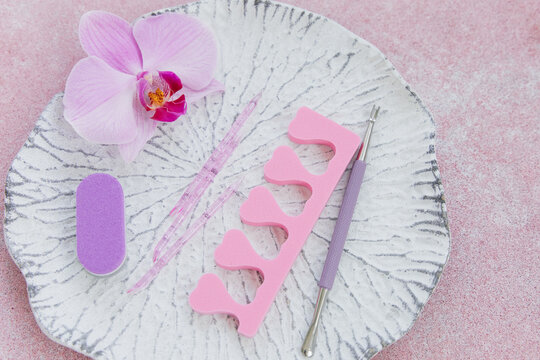 Manicure tools and pink orchid flower placed on a white textured plate against a pink background