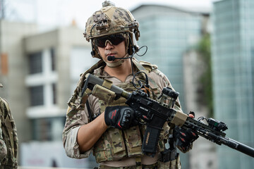 Fototapeta premium A soldier stands ready outdoors, holding a rifle with focused concentration and determination while tactical gear equips the individual for combat readiness in an urban location.