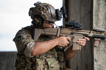 Fototapeta premium A tactical soldier holds a modern rifle with intense focus while aiming around a concrete corner, conveying a sense of vigilance, readiness, and strategic defense.