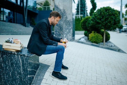 Job failure grief makes laid off worker look down on staircase holding cold alcohol bottle.