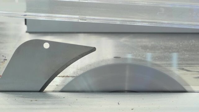 Close-up of circular saw blade spinning. Motion blur reveals sharp teeth and central hole. Sawdust forms as it cuts wood. work surface is smooth and metallic