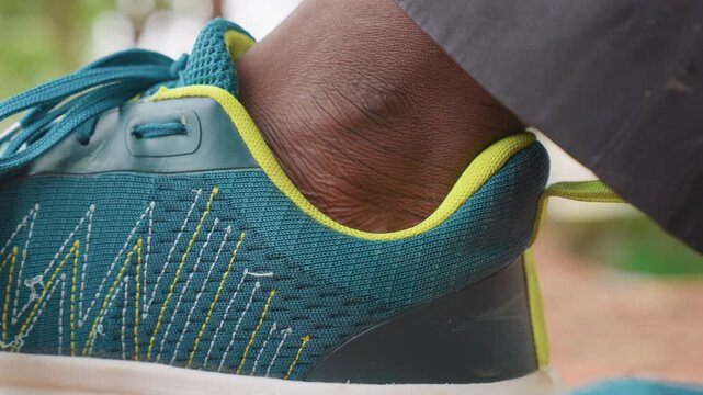 Close up shots focus on ankle in teal sportswear with yellow accents. subject wears blue athletic sneaker featuring white and yellow stitching patterns highlighting shoe texture details