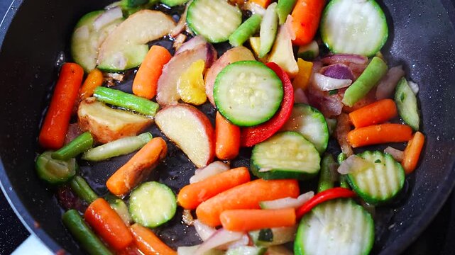 In a dark nonstick pan, stir fried vegetables shimmer in a layer of hot oil, zucchini, carrots, potatoes and green beans cooking evenly from above, concept of quick homemade lunch