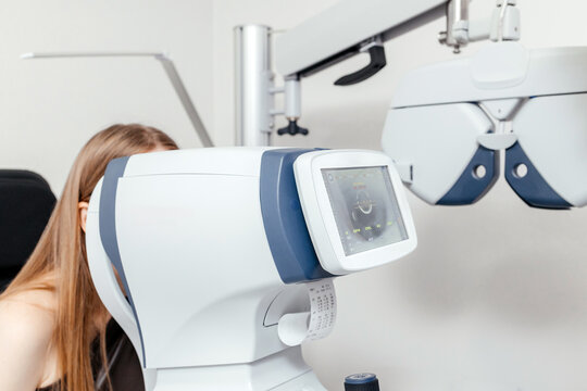Female patient taking an automated vision and refraction test using autorefractor equipment in a modern optometry and ophthalmology clinic.