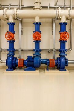 Industrial pump manifold system with blue pipes and orange valves. Mechanical water circulation and pressure booster infrastructure in utility room
