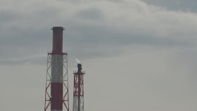 Low angle view of tall red and white factory chimneys reaching into cloudy sky in Tomakomai, Hokkaido, Japan. Fixed 4K video.
