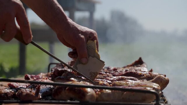Hand turning meat, offal and chorizo sausages on smoky grill, traditional Argentine asado, slow motion