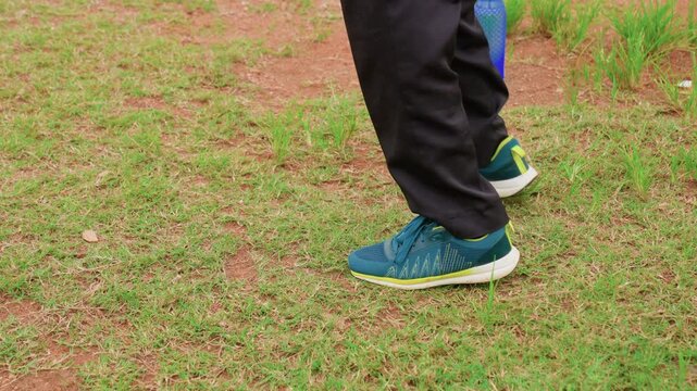 Person blue running shoes with black pants standing still or moving slightly outdoors. ground is patchy green and brown suggesting outdoor training environment