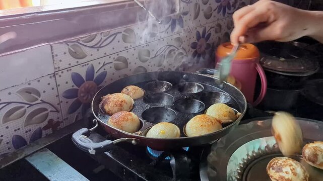 Closeup of south indian dish paddu or savory rice and lentil dumplings being carefully flipped inside a hot pan