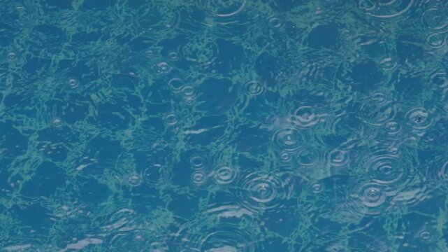 Close up view of pattern of ripples created by raindrop on the surface of a swimming pool with blue tiles.