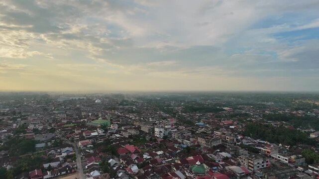 Panoramic aerial perspective of a vast residential townscape with compact houses and winding streets as day turns to night. Sunset sky with clouds, city lights starting to glow