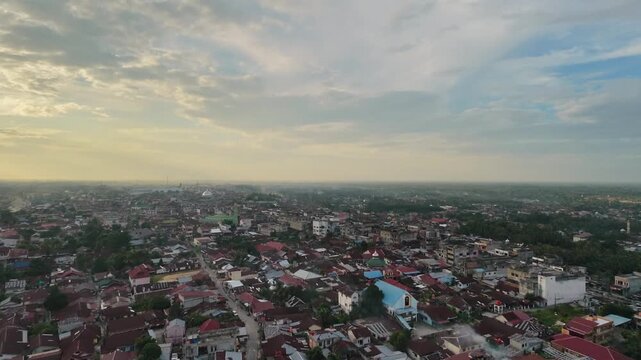 Panoramic aerial perspective of a vast residential townscape with compact houses and winding streets as day turns to night. Sunset sky with clouds, city lights starting to glow