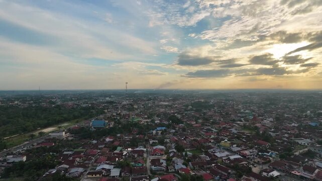 Aerial view of a small town settlement during sunset, with houses and buildings under a dramatic cloudy sky. Urban landscape, evening twilight, and community travel concept.