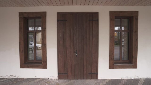 Rustic wooden door and framed windows on white stucco house facade, static exterior architectural view with covered porch and paved entrance