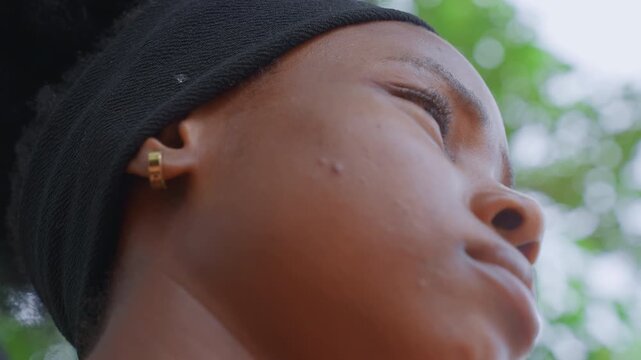 Close up view focusing on side angle details of young adult woman face profile. subject wears black headband and small gold hoop earrings with natural skin texture visible. Background shows