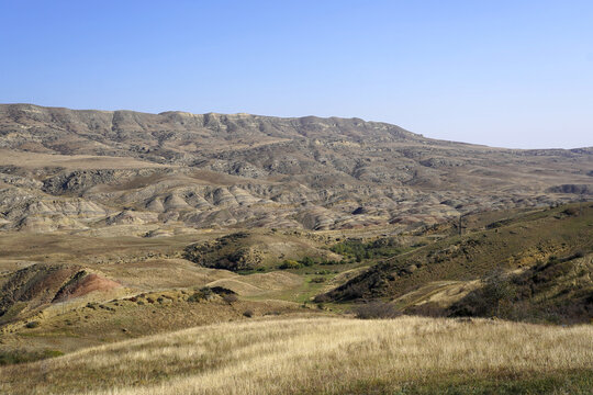 A sweeping view overlooks the eroded sedimentary ridges, colorful badlands, and arid steppe terrain near Udabno and the Davit Gareja region in eastern Georgia