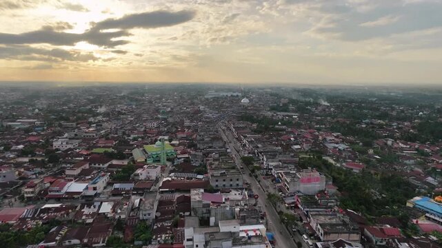 Aerial view of a densely populated town with countless red-roofed houses and buildings stretching to the horizon under a dramatic cloudy sunset sky. Urban landscape and evening atmosphere