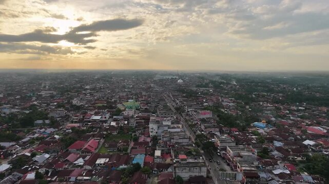 Aerial view of a densely populated town with countless red-roofed houses and buildings stretching to the horizon under a dramatic cloudy sunset sky. Urban landscape and evening atmosphere