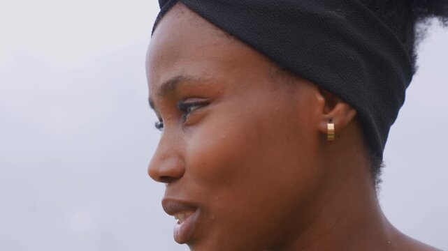 Close up profile shots of woman with natural hair wearing minimal jewelry gold hoop earring against overcast sky. subject features and accessories are emphasized by soft lighting