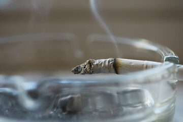 Naklejka na ściany i meble Smoking Addiction Concept: Burning Cigarette in an Ashtray with Rising Smoke Indoors