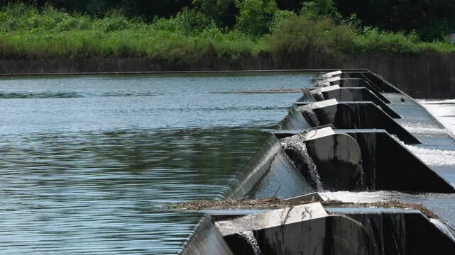 Wide View of Water Overflowing River Weir with Green Forest Background 4K