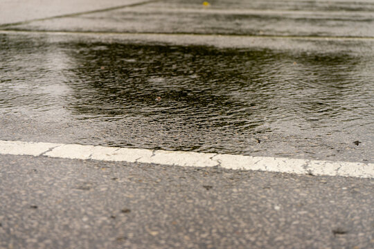 Rain falling into a puddle beside a white road marking