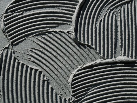 Close up of grey tile glue on floor. Notched trowel creates parallel ridges in wet cement mortar. Construction material texture for tiling work home renovation. Surface shows pattern of adhesive used