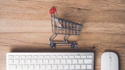 Miniature shopping cart on wooden desk next to computer keyboard and mouse representing ecommerce online shopping internet retail consumer buying and digital trade © MohamadFaizal