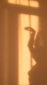 Young woman performs a soft feminine dance with her hands and body, seen as a graceful sunset shadow on the wall