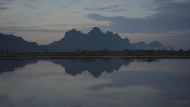 A tranquil view of jagged mountain silhouettes casting a perfect mirror reflection across the still surface of a lake under a soft evening sky