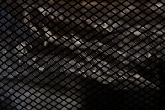 Abstract background of black metal diamond mesh grid pattern over silver foil texture.
