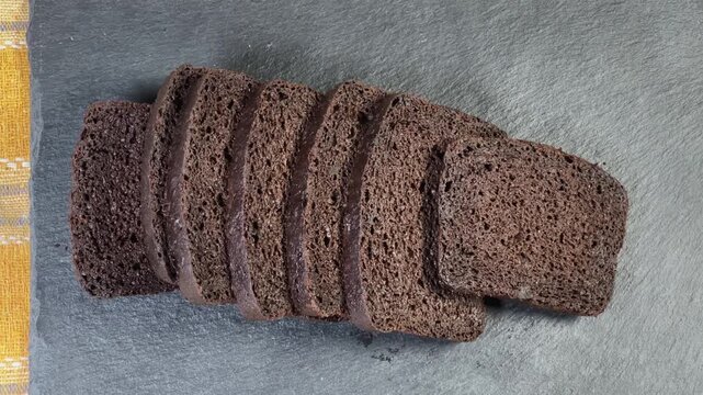 Sliced brown bread on black flat slate plate, top view