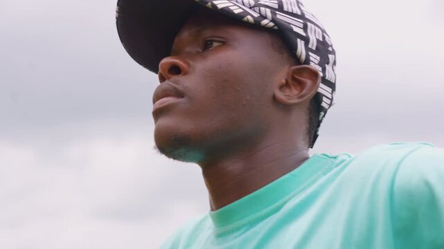 Close up portrait captures side profile of young adult male with short hair wearing black patterned cap and mint green shirt. subject ear neck and part of his shoulder are visible as man