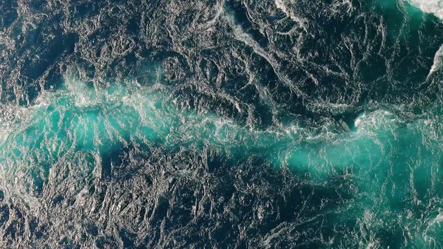 Dynamic overhead view of churning turquoise water current flowing with turbulent waves.