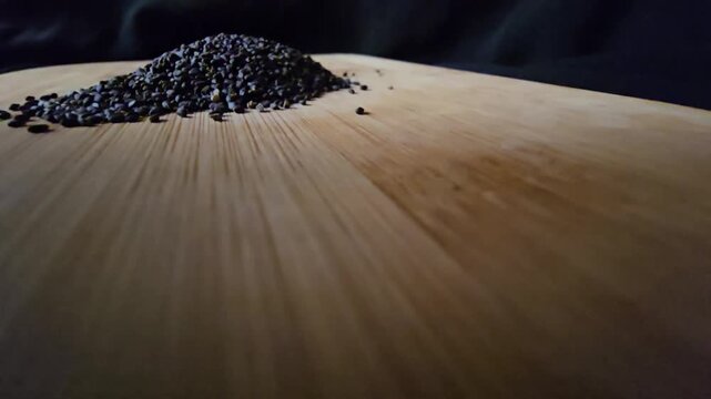 Low-angle wide macro video of a neat pile of organic black basil seeds on a textured wooden board. Ideal for health food, cooking, and natural wellness concepts.   