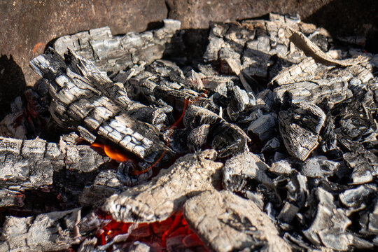 Smoldering charcoal and glowing red embers in a metal fire pit close up
